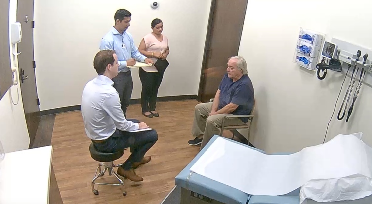 man sitting in doctors office and students standing next to him